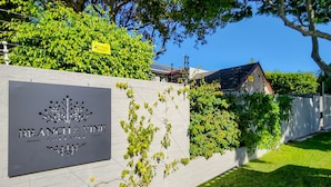 A sign for 'Branch & Vine Cottages' with a white wall and greenery. - Clivia - Pinoak Self-catering Cottages (Cape Town)