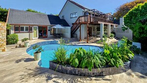 Ein zweistöckiges Haus mit Swimmingpool, überdachter Terrasse und Steinmauer.