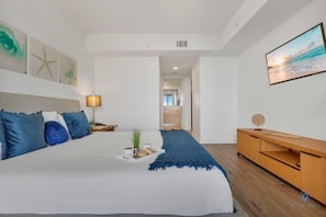 A modern bedroom with a large bed, a TV, a wooden console, and a view of the sea.