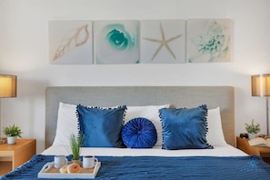 Una cama bien tendida con ropa de cama azul y blanca, una bandeja con alimentos para el desayuno y una decoración con forma de estrella de mar en la pared.