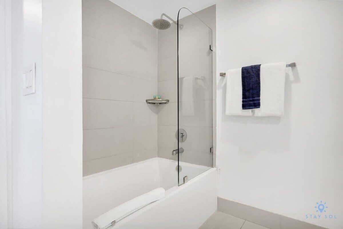 Een moderne badkamer met een douchecabine van glas, een witte badkuip en een handdoekrek met een blauwe handdoek.