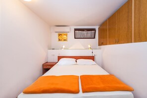 A bedroom with a bed, two bedside tables, a nightstand, a wardrobe, an air conditioning unit, and a window with curtains.