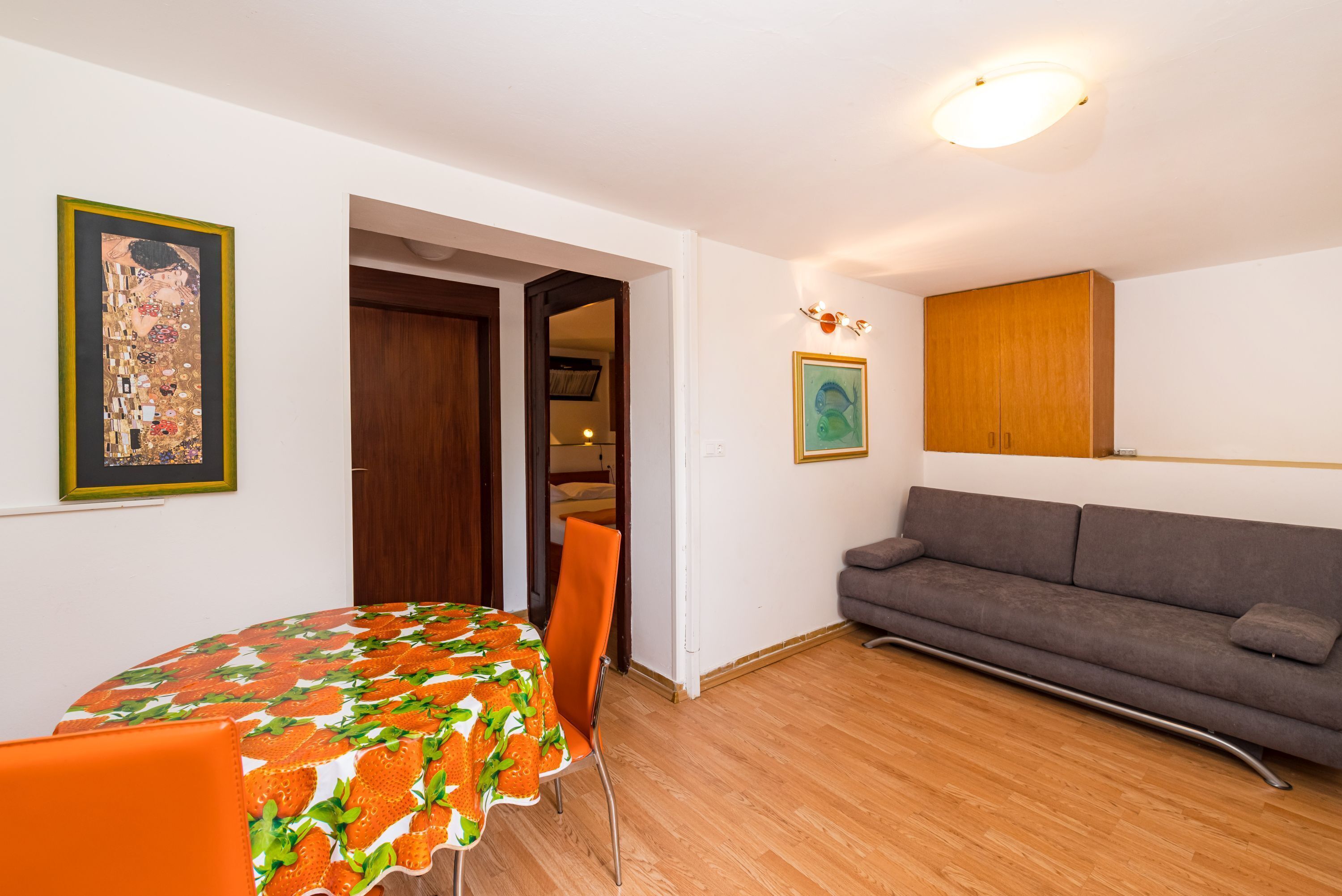 A room with a dining table, chairs, a sofa, and two framed artworks on the walls.