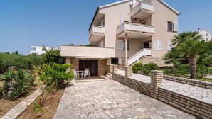 A multi-story residential building with a stone-paved courtyard, outdoor seating, and a staircase leading to the upper floors. - Apartment Ljubica With Nice Garden 2 (Novalja)