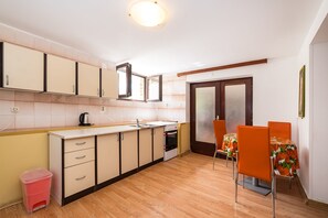 A compact kitchen with a sink, stove, and cabinets, a dining area with orange chairs, and a small trash bin. - Apartment Ljubica With Nice Garden 2 (Novalja)
