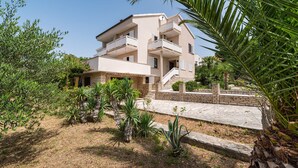 A multi-story building with balconies, surrounded by greenery and a stone pathway. - Apartment Ljubica With Nice Garden 2 (Novalja)