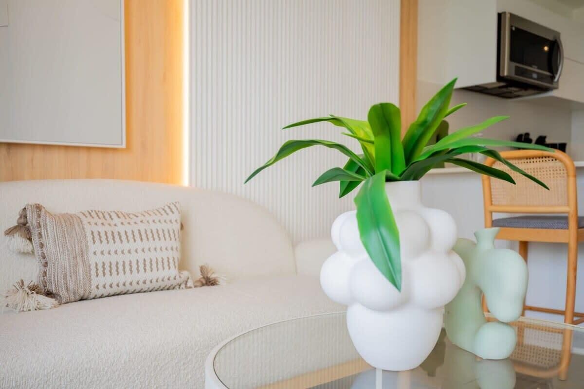 Una sala de estar moderna con un sofá blanco, un jarrón blanco decorativo con hojas verdes y una silla de mimbre.