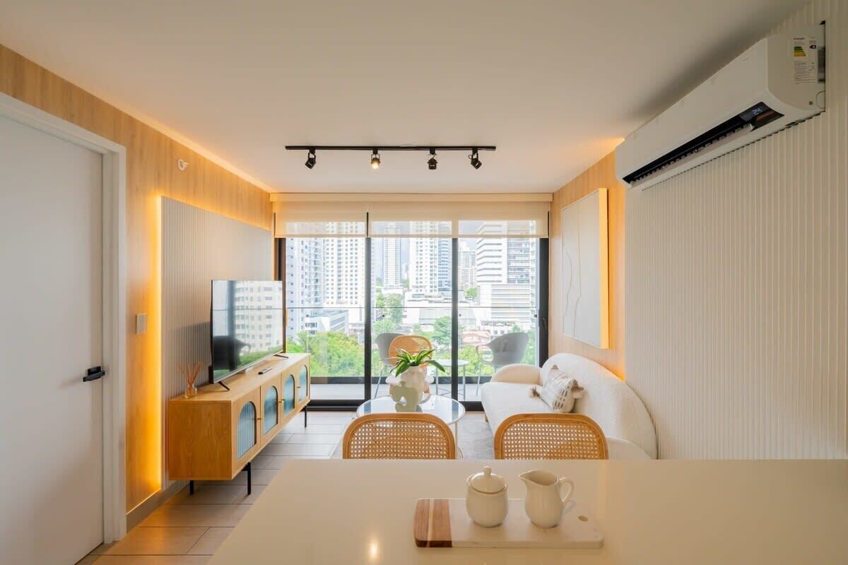A modern living room with a sofa, a coffee table, and a TV. There is a large window with a city view.