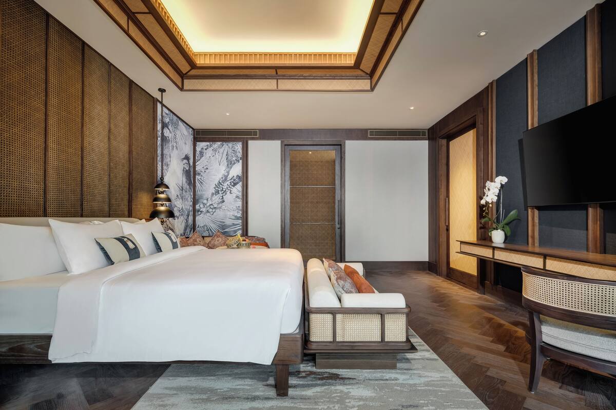 A modern bedroom with a large bed, a sofa, a flat-screen TV, and a decorative wall panel.