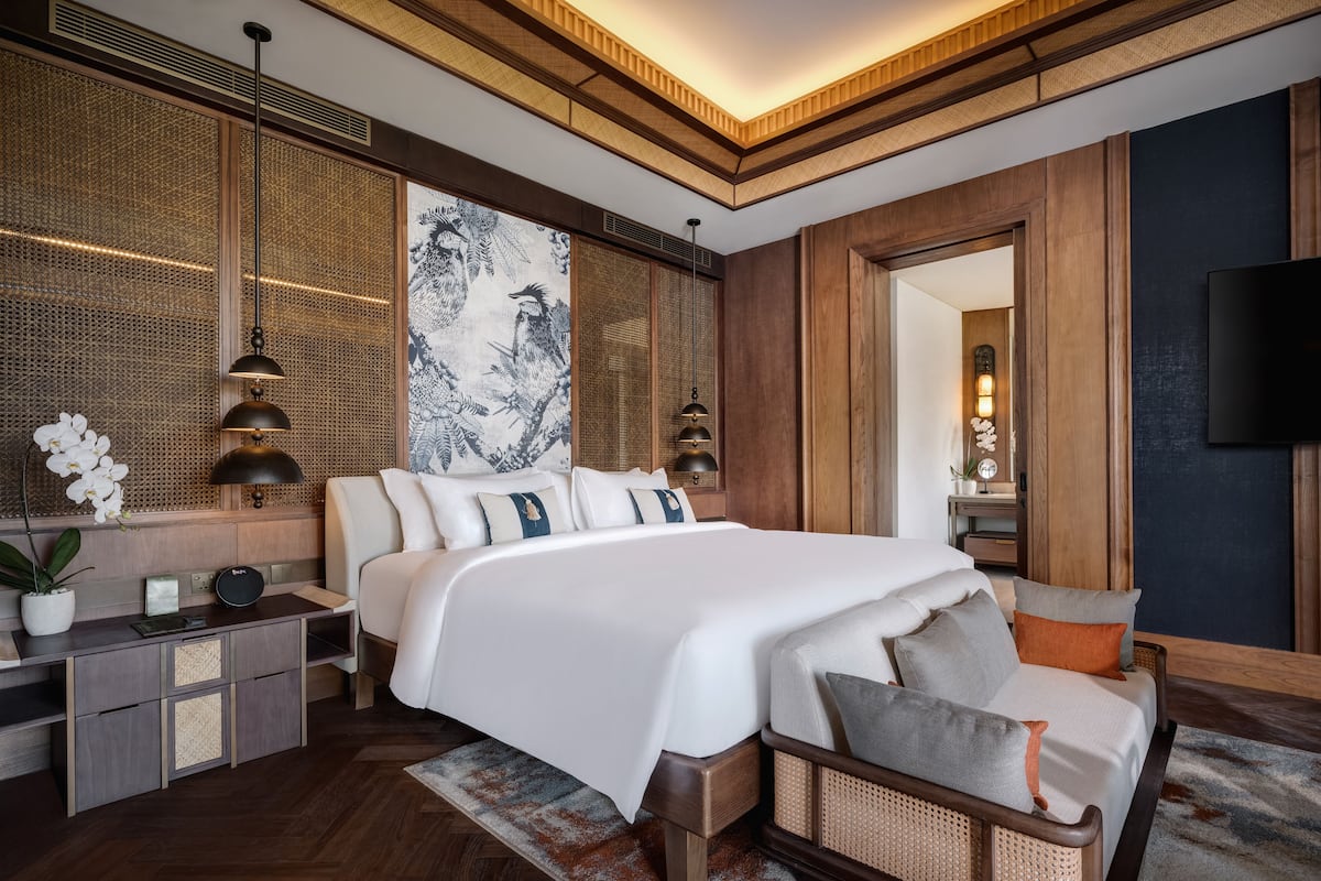A modern hotel room with a large bed, bedside tables, a TV, and a large artwork on the wall.