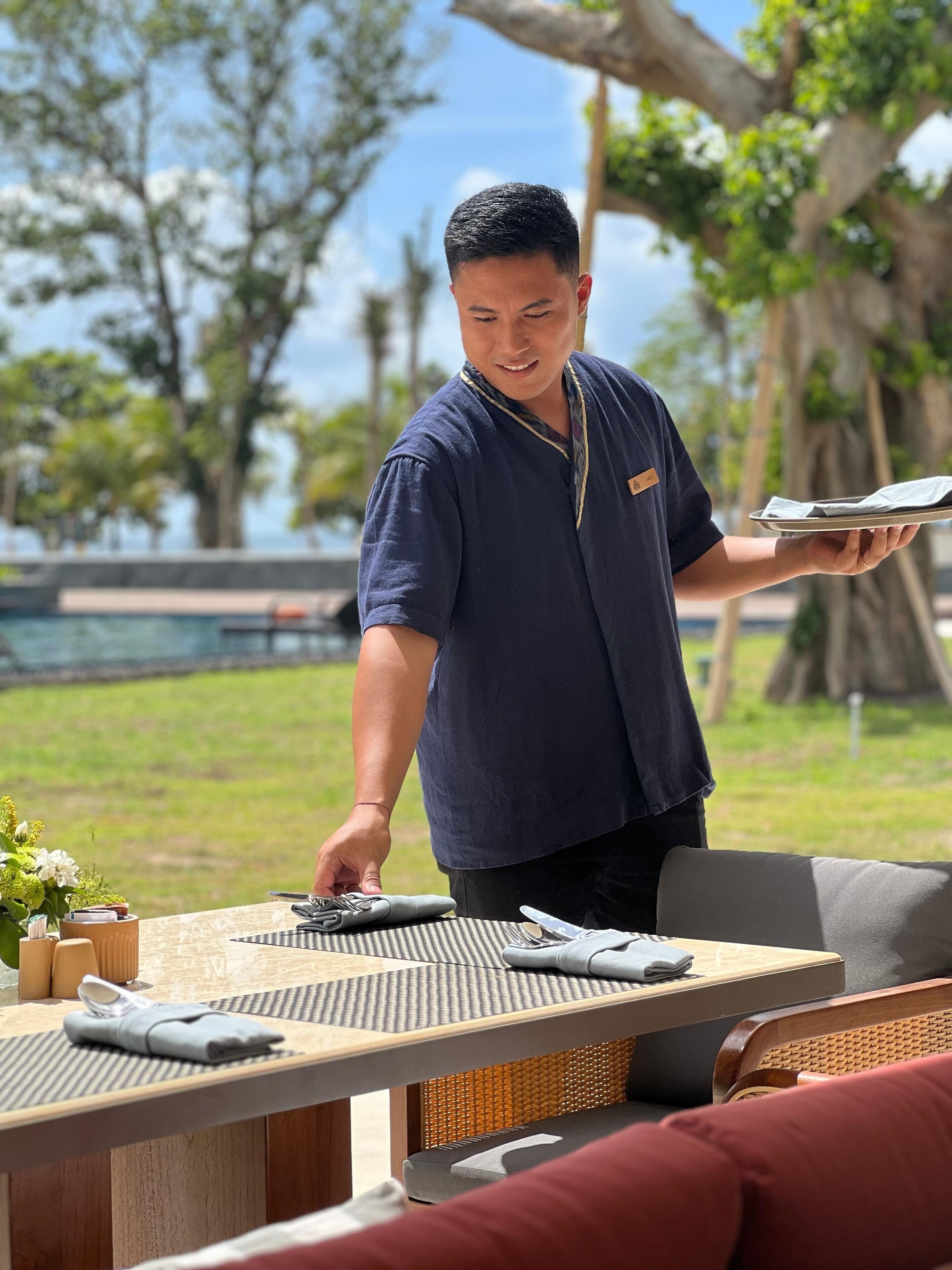 Una persona sirviendo comida en una mesa al aire libre, con vista a una piscina y árboles.