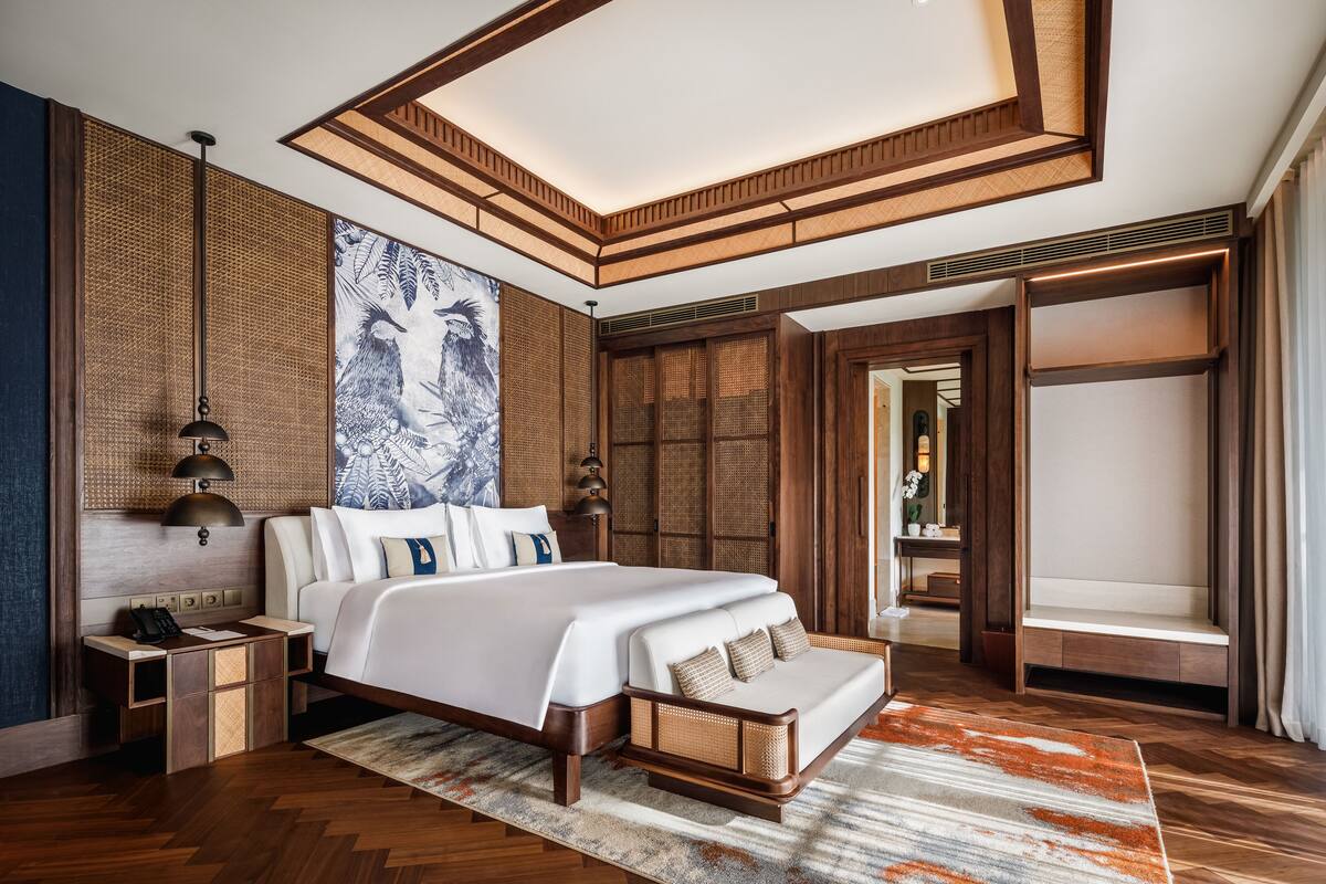 A modern hotel bedroom with a large bed, wooden headboard, and a view of the hallway.