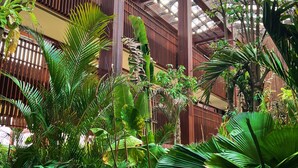A spacious atrium with high ceilings and a glass roof, surrounded by lush tropical plants and wooden beams. - The Meru Sanur (Denpasar)