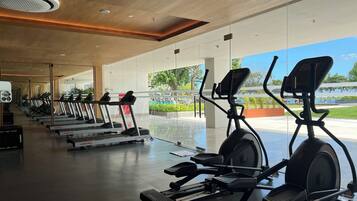 A modern gym with treadmills, elliptical machines, and a large glass wall offering a view of an outdoor area.