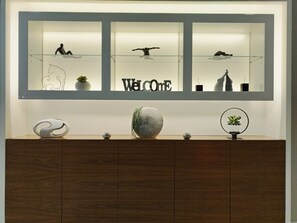 Una recepción con un cartel de 'Welcome', vitrinas de vidrio con esculturas y un mueble de madera debajo.