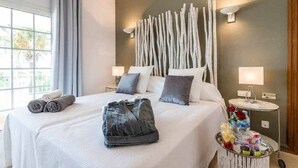A hotel room with a large bed, two bedside lamps, a small table with a lamp, and a window with curtains. - Beautiful  Villa Near ibiza Town and Talamanca Beach (Santa Eulària des Riu)