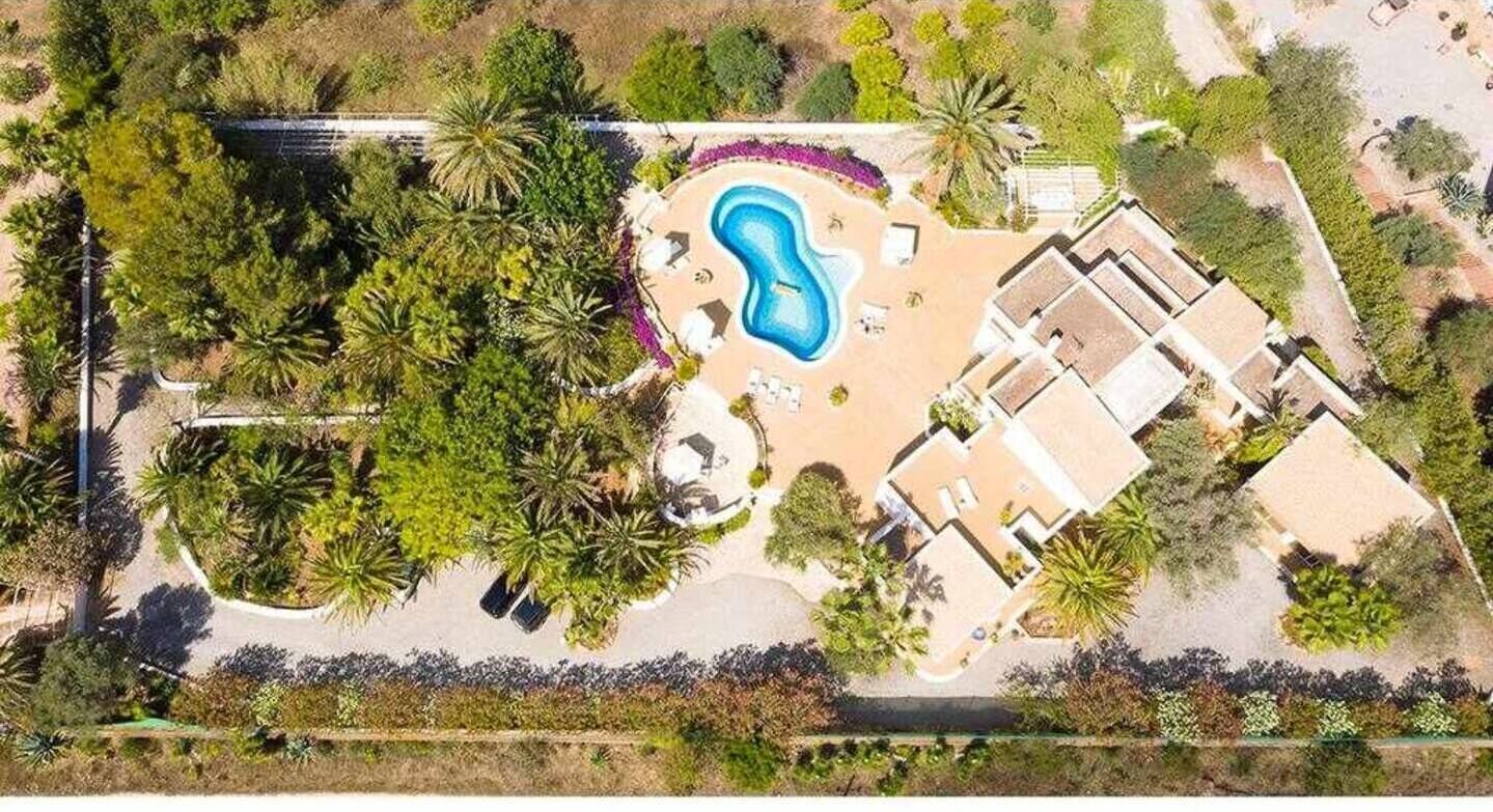 Luftaufnahme eines Resorts mit einem Schwimmbecken, umgeben von Palmen und einem Gebäude mit flachem Dach.