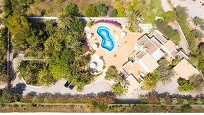 An aerial view of a resort with a swimming pool surrounded by palm trees and a building with a flat roof. - Beautiful  Villa Near ibiza Town and Talamanca Beach (Santa Eulària des Riu)