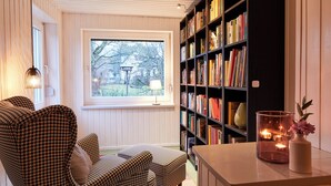 A cozy reading nook with a houndstooth patterned chair, a bookshelf filled with books, and a candle on a table.