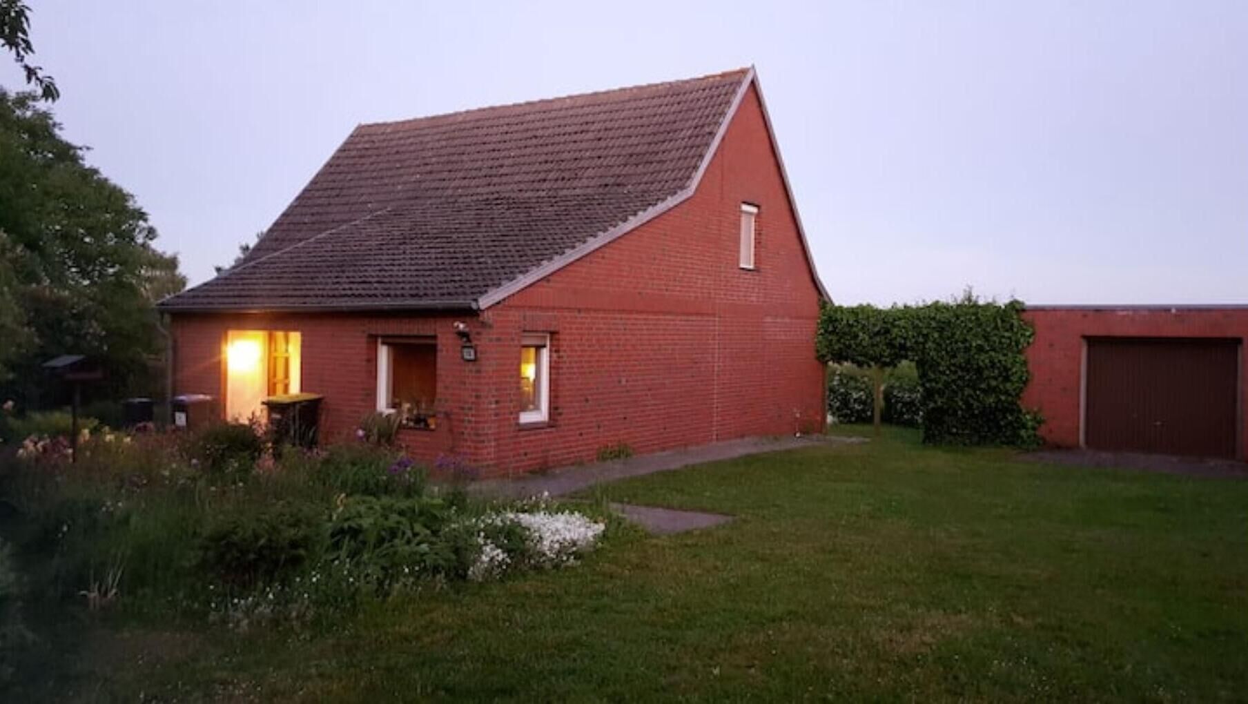 Une maison en briques rouges, avec un toit en pente, un petit porche et un jardin bien entretenu.