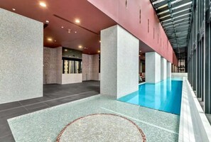 A modern indoor swimming pool with a clear water feature, surrounded by a tiled floor and walls with a textured finish.