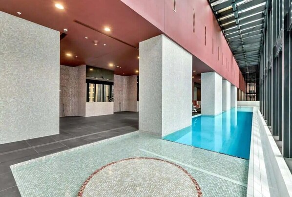 Una piscina interior moderna con un elemento acuático cristalino, rodeada de un suelo y paredes alicatados con textura.