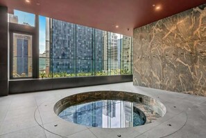A modern indoor pool area with a glass enclosure, a marble wall, and a view of high-rise buildings. - A Chic 2BR Apt Near Melbourne CBD w/ FREE Parking (Melbourne)
