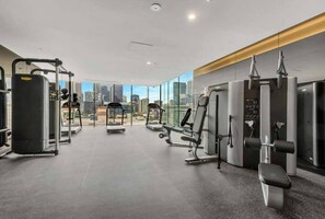 A modern gym with various exercise equipment, large windows offering a city view, and a clean, spacious layout. - A Chic 2BR Apt Near Melbourne CBD w/ FREE Parking (Melbourne)