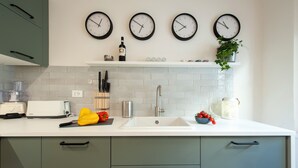 A kitchen with a white countertop, green cabinets, a white sink, and three wall clocks. - Canto Rivolto - Flo Apartments (Firenze)