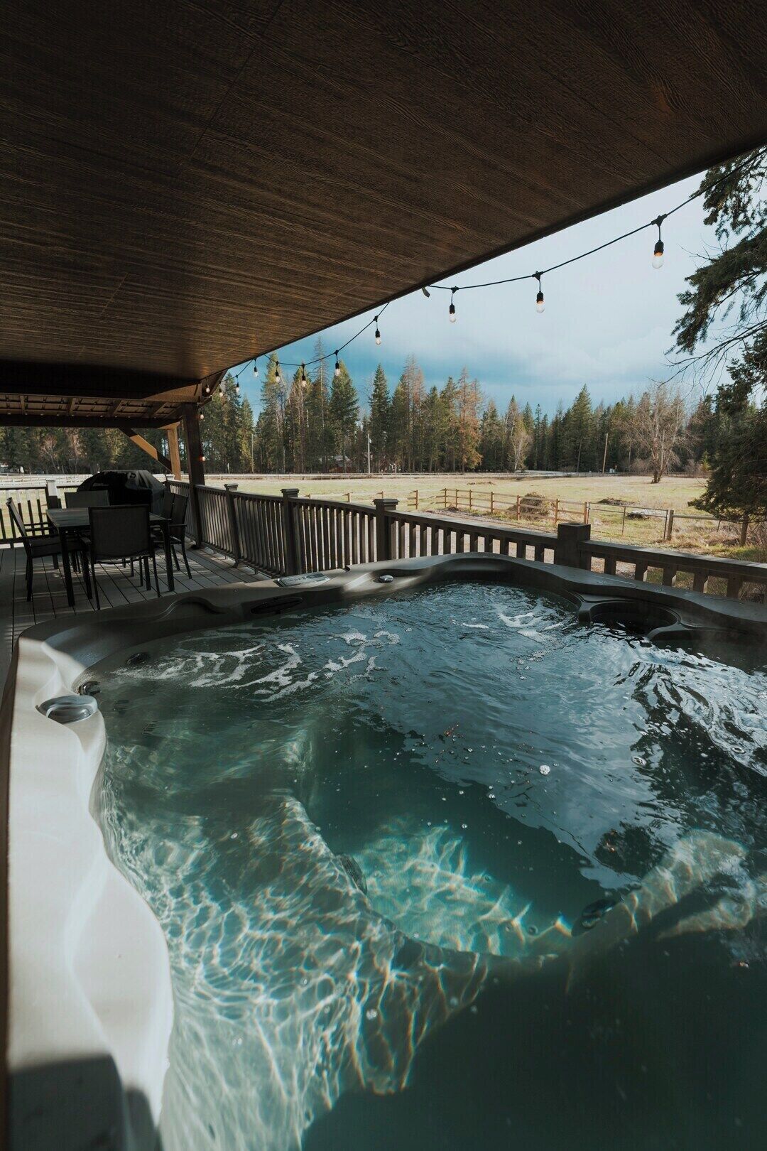 Un jacuzzi bajo una pérgola de madera con vista a un área boscosa.