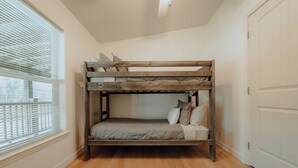 Een stapelbed met houten frame en matras in een kamer met houten vloer en raam met jaloezieën.