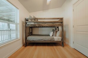 A bunk bed with a wooden frame and a mattress in a room with wooden flooring and a window with blinds. - Farmhouse - Peaceful 5 bedroom / 3 bath (Whitefish)