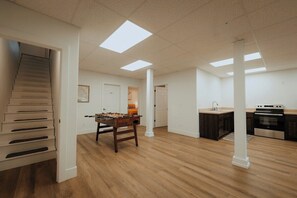 A spacious living area with a wooden floor, a foosball table, a kitchen with dark cabinets and a stove, and a staircase.