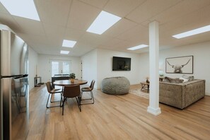 A modern kitchen with a dining area, a large bean bag, and a sofa with a mounted artwork.