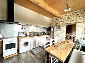 A compact kitchen with a stove, washing machine, and a dining area with a wooden table and chairs.