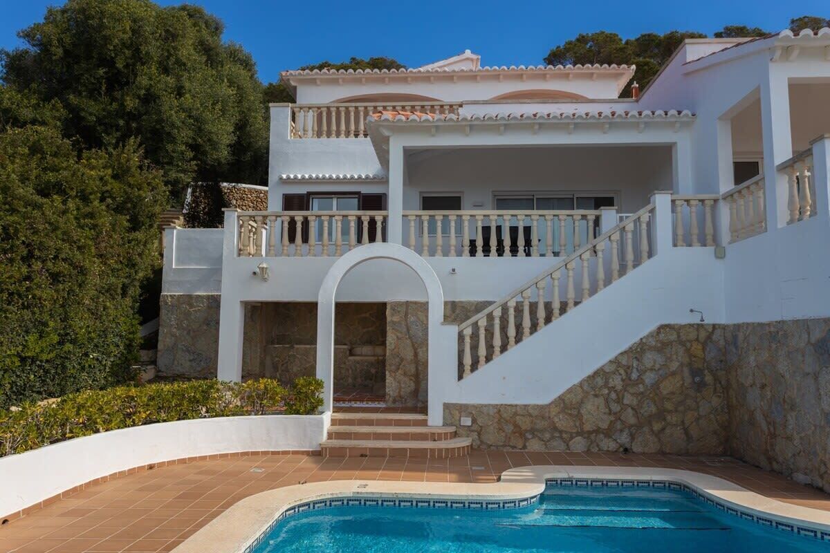 A two-story house with a swimming pool, stone walls, and a balcony.