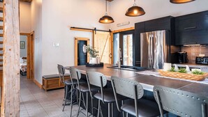 Una cocina moderna con una isla central, taburetes de bar, iluminación colgante y electrodomésticos de acero inoxidable.