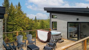 Una terraza moderna al aire libre con sillas Adirondack, un jacuzzi y un área de spa con paredes de vidrio.