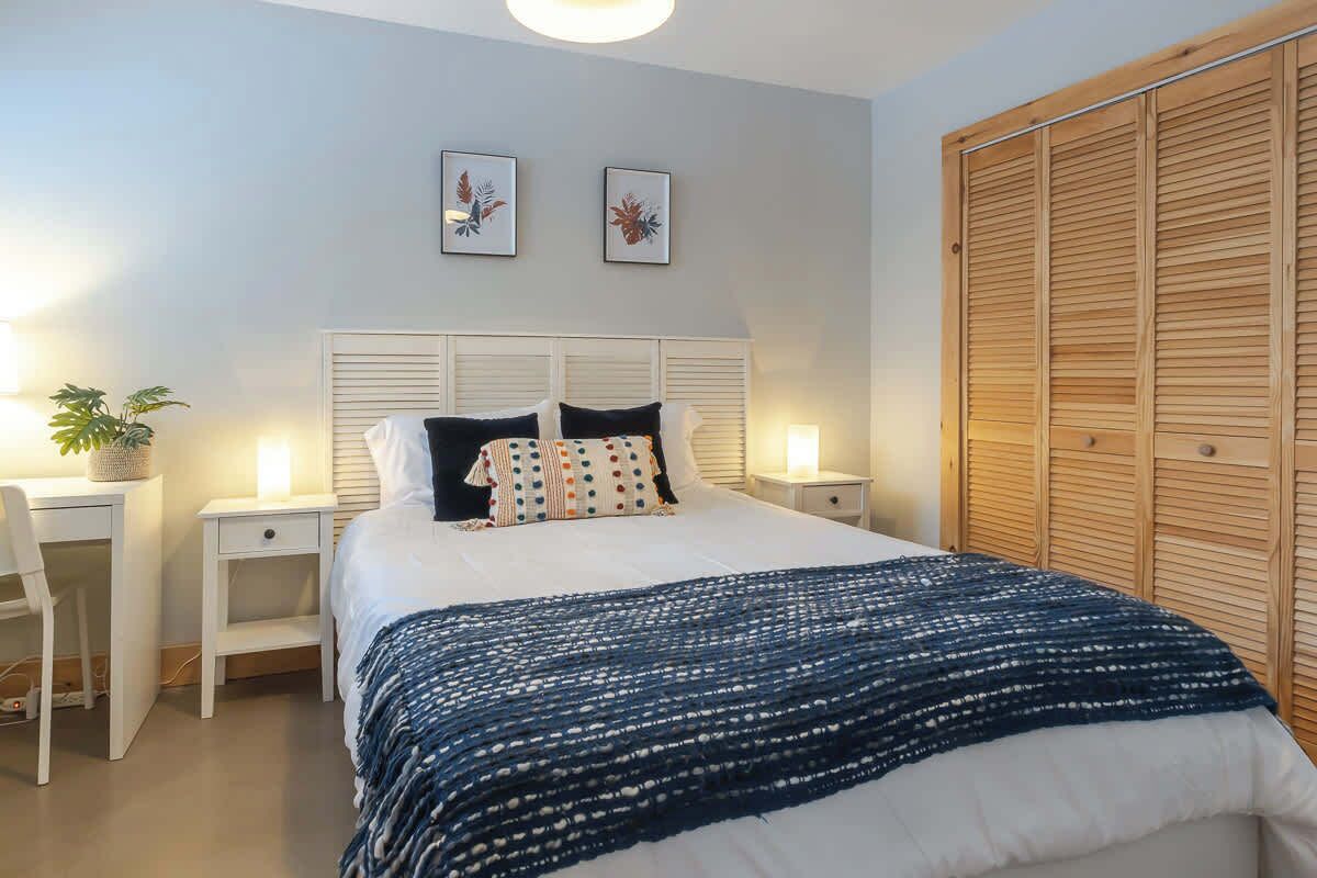 Een slaapkamer met een bed, nachtkastjes, een bureau en een kledingkast.