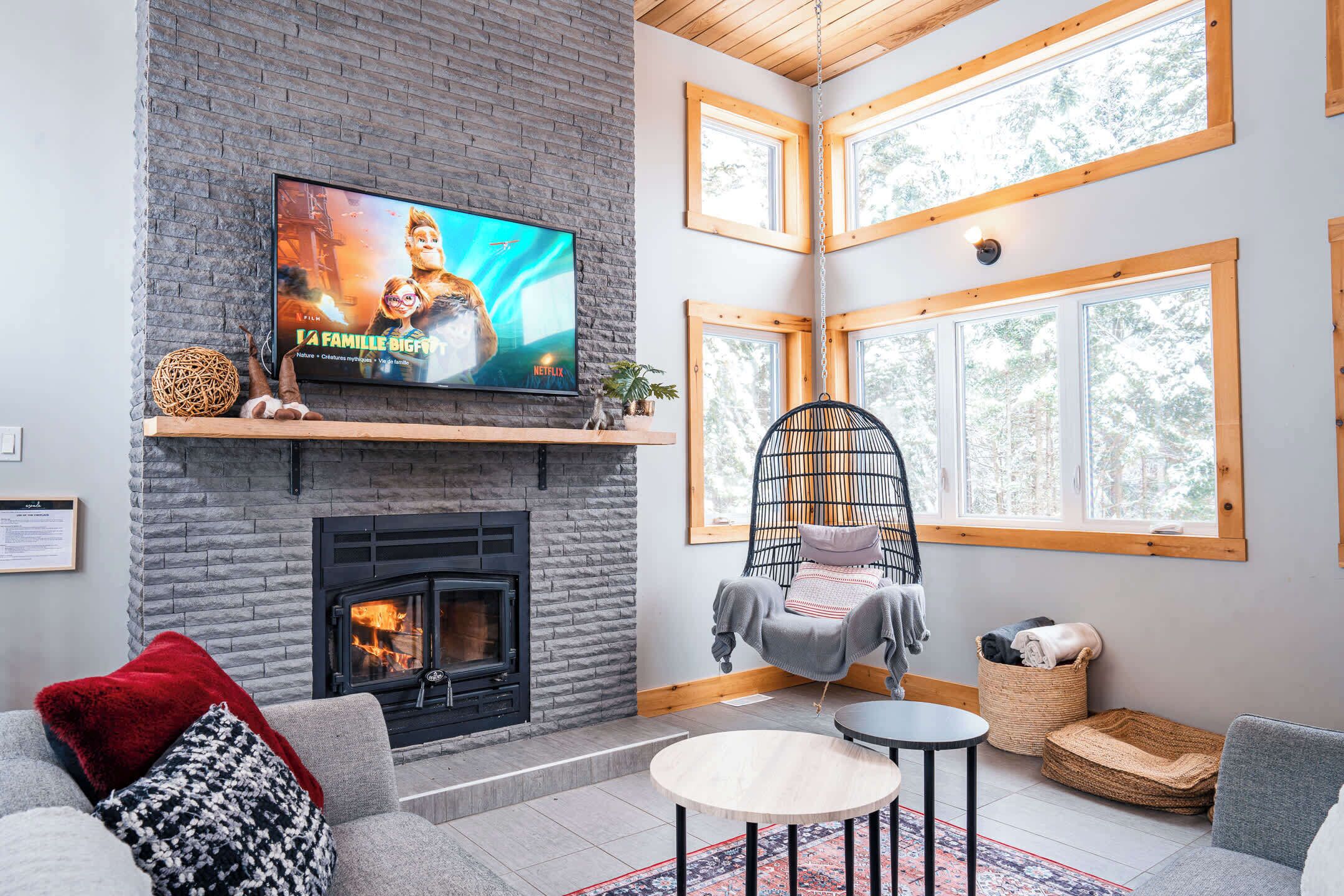 A cozy living room with a fireplace, a television displaying a movie, and a hanging chair.