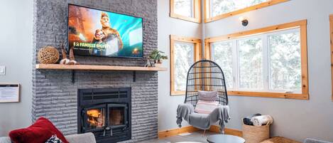 A cozy living room with a fireplace, a television displaying a movie, and a hanging chair.