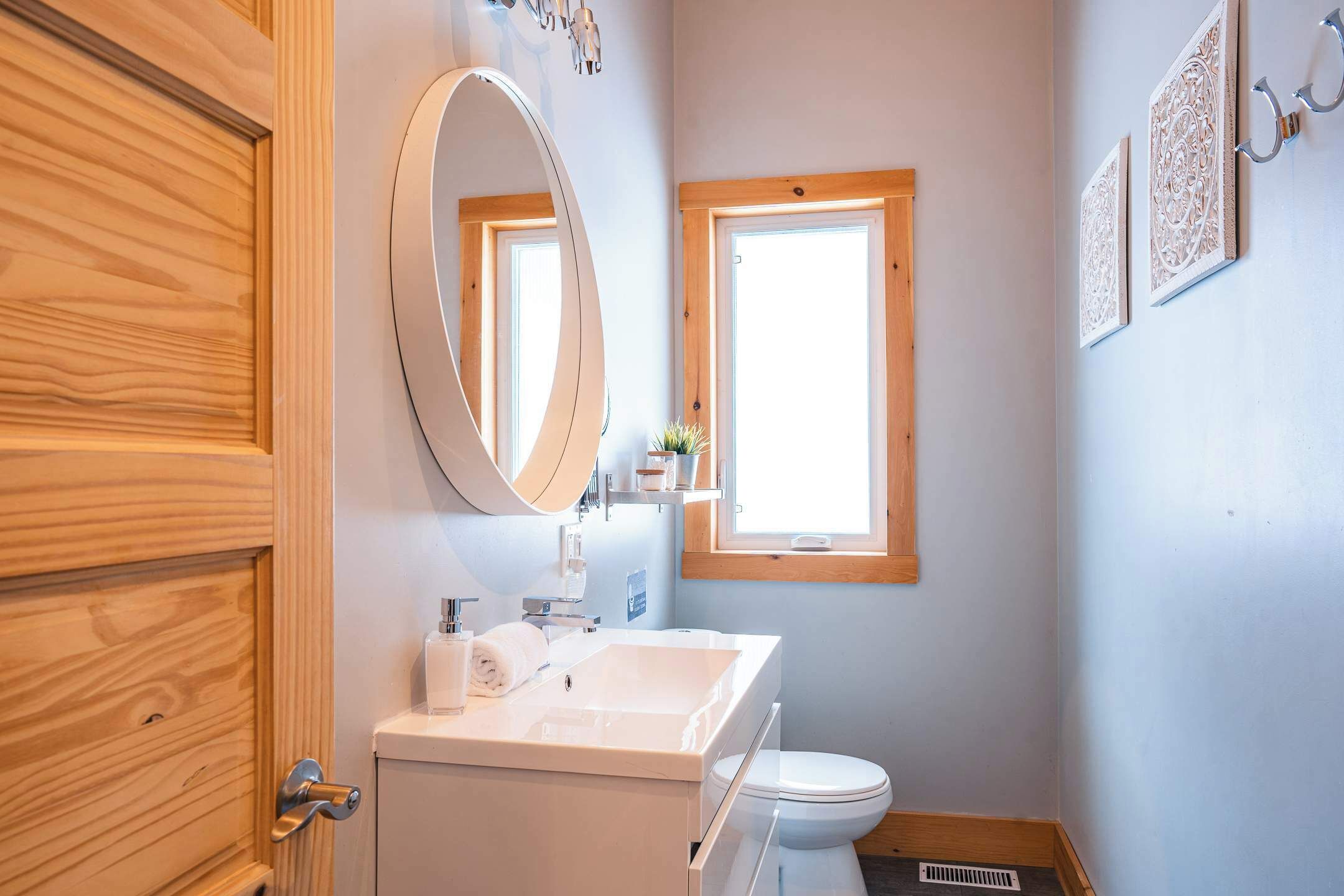 A bathroom with a wooden door, a white sink, a mirror, a window, and a toilet.