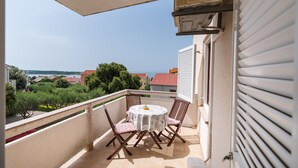 A balcony with a table and chairs, a view of the sea, and a building with a red roof. - Apartment Ljubica With Nice Garden 3 (Novalja)