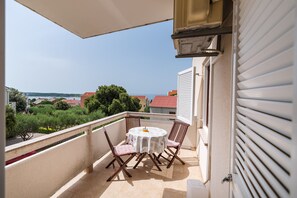 A balcony with a table and chairs, a view of the sea, and a building with a red roof. - Apartment Ljubica With Nice Garden 3 (Novalja)