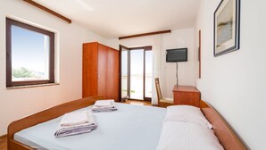 A bedroom with a bed, a TV, a wooden wardrobe, and a door leading to a balcony. - Apartment Ljubica With Nice Garden 3 (Novalja)