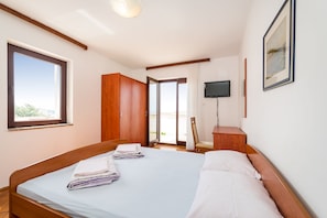 A bedroom with a bed, a TV, a wooden wardrobe, and a door leading to a balcony. - Apartment Ljubica With Nice Garden 3 (Novalja)