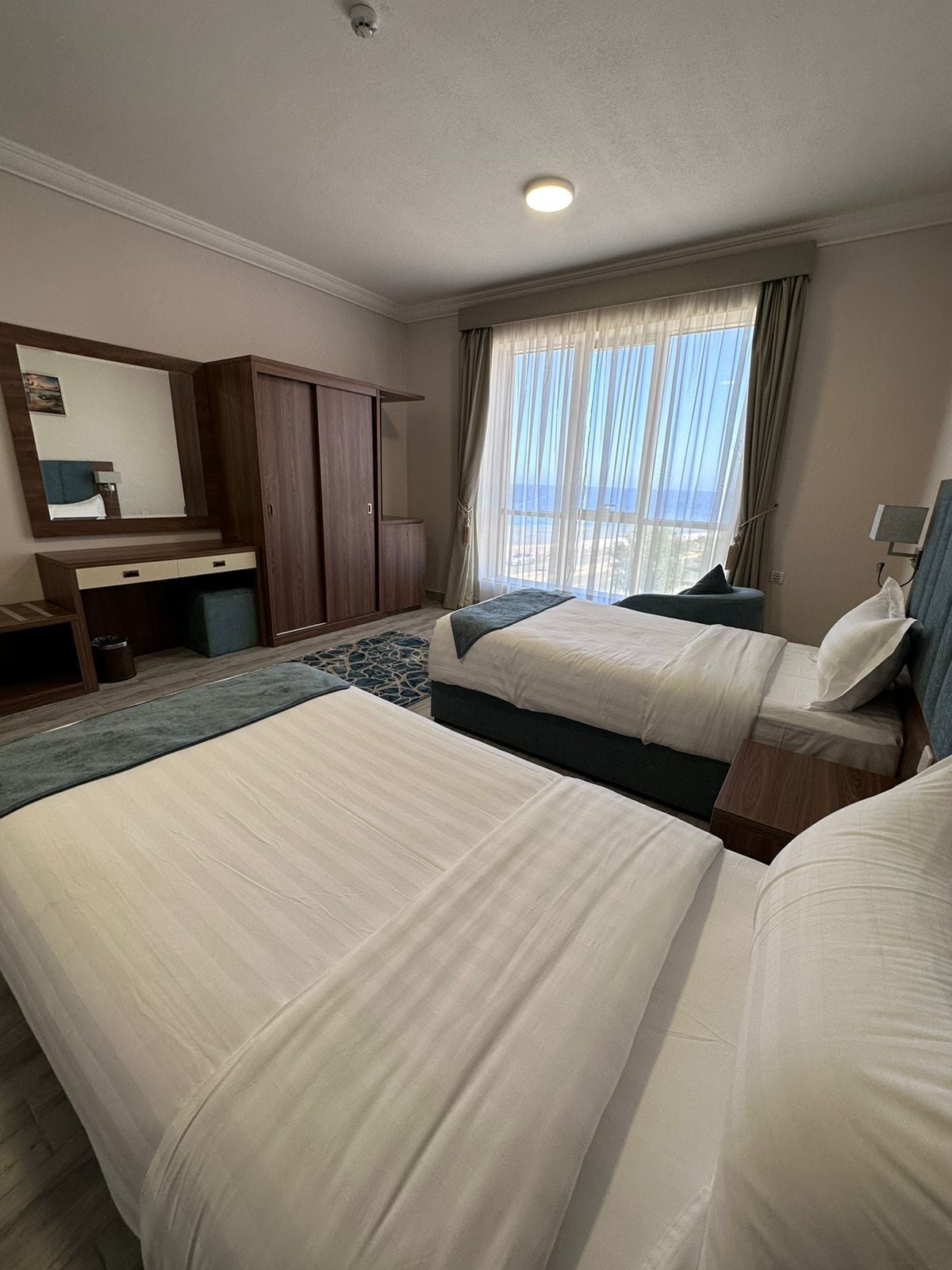 Habitación de hotel con dos camas, un escritorio, un armario y un amplio ventanal con vistas.