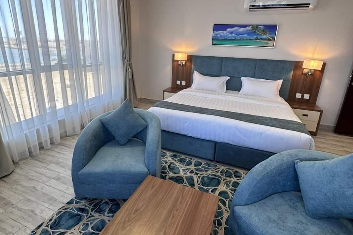 A hotel room with a bed, two armchairs, a coffee table, and a painting on the wall.