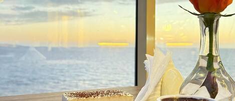 A dessert tray with a slice of cake and a cup of coffee on a wooden table near a window overlooking a body of water.