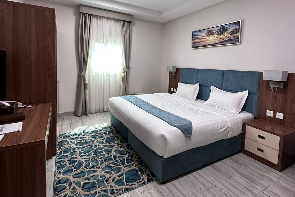 A hotel room with a large bed, a desk, a wardrobe, and a window with curtains.